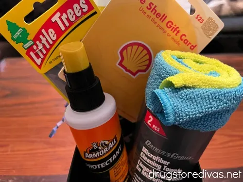 A Shell gas station gift card, air freshener, Rain X, ArmorAll, and a microfiber towel, plus, blue paper shred, in a car cup organizer.