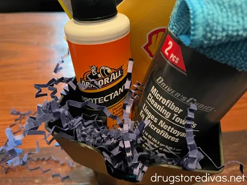 An air freshener, Rain X, ArmorAll, and a microfiber towel, plus, blue paper shred, in a car cup organizer.