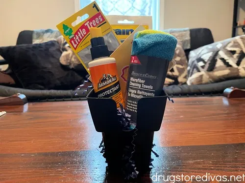 An air freshener, Rain X, ArmorAll, and a microfiber towel, plus, blue paper shred, in a car cup organizer.