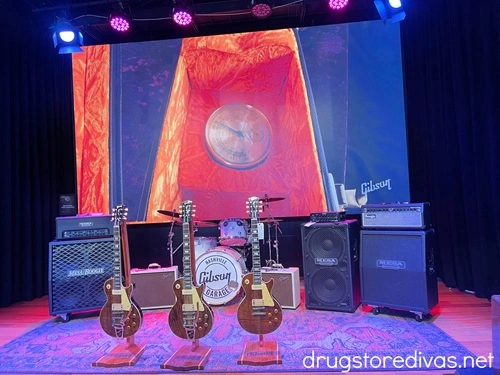 The stage inside the Gibson Garage in Nashville, which has speakers and three guitars on it.