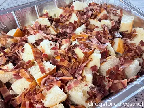 Pieces of bacon on top of bread cubes in an aluminum pan.