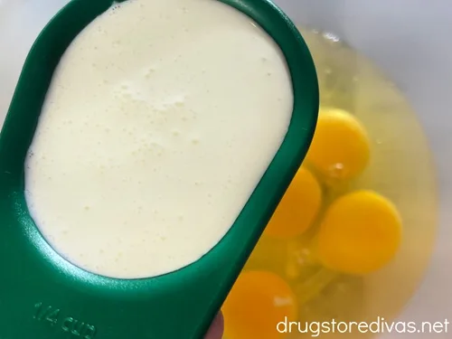 Heavy cream in a measuring cup above a bowl of eggs.