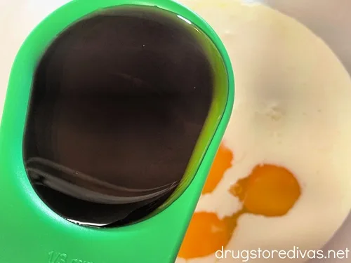 Maple syrup in a measuring cup above a bowl of eggs.