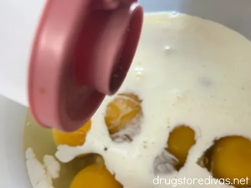 Salt being poured into a bowl with eggs and heavy cream in it.