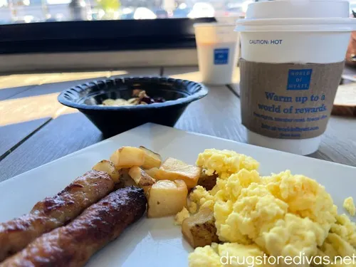 Breakfast at Hyatt Place in Nashville, which is sausage, home fries, and scrambled eggs on a plate with yogurt in a black bowl and two coffee cups in the background.