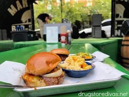 A burger with macaroni and cheese on a tray with more behind it on a green table with a stage behind it at Martin Bar-B-Que Joint in Nashville.