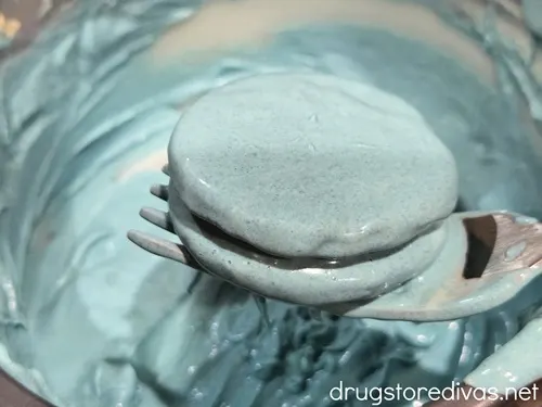 A blue Oreo cookie being pulled out of melted blue chocolate by a fork.