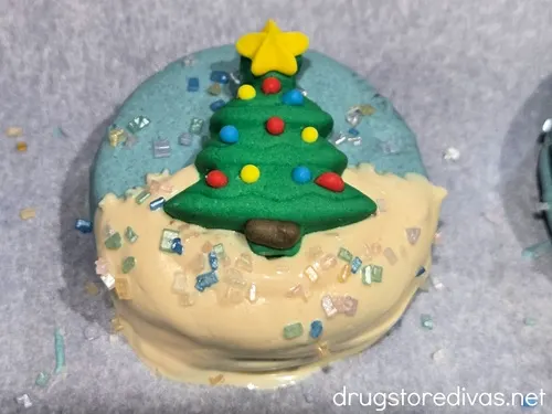 A blue and white Oreo cookie with a large Christmas tree candy and sugar sprinkles on it.