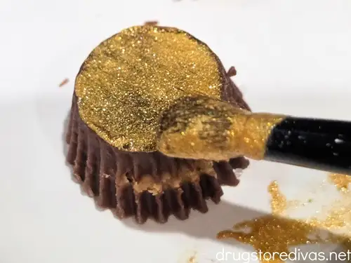 A mini Reese's peanut butter cup being brushed with gold glitter.