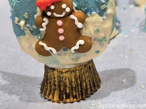 An Oreo cookie decorated to look like a snow globe with a female gingerbread cookie in it.