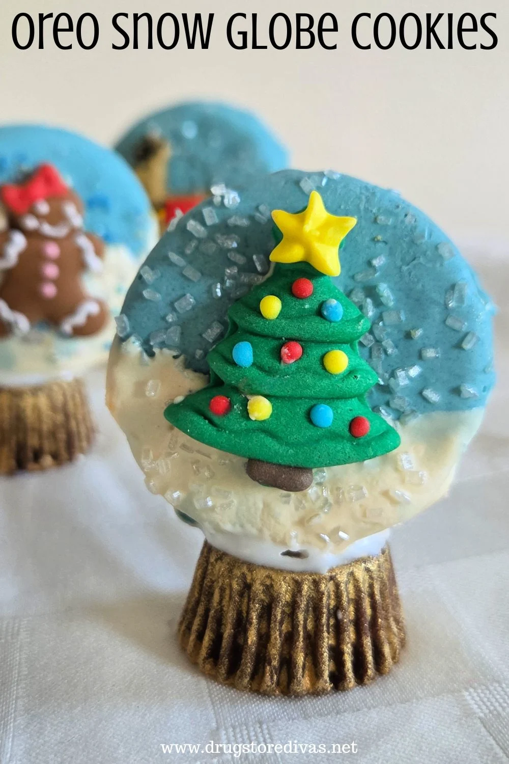 An Oreo cookie decorated to look like a snow globe with a Christmas tree in it, with two other cookies behind it, and the words 