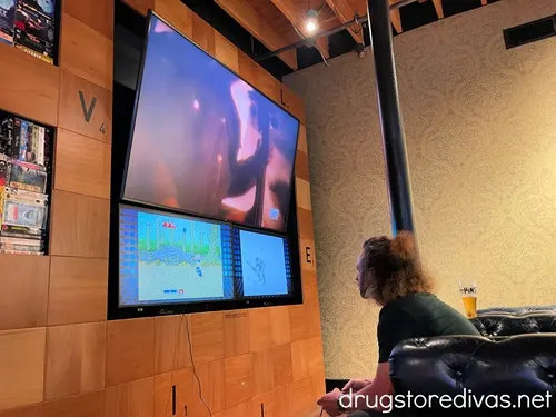 A man playing video games and looking at three TVs at 16 Bit Bar+Arcade in Nashville.
