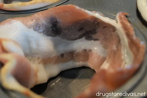 A piece of bacon in the cavity of a muffin tin.