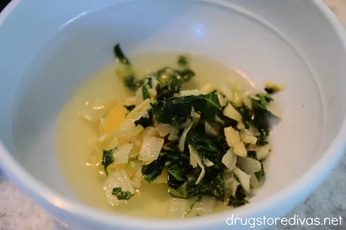A cracked egg topped with green vegetables in a blue bowl.