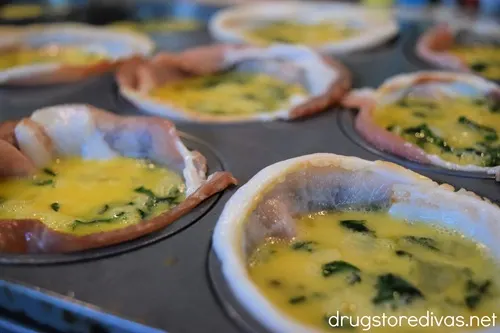 Uncooked bacon-wrapped egg cups in a muffin tin.