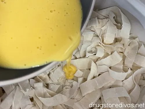 Yellow custard in a bowl being poured over strips of phyllo dough.