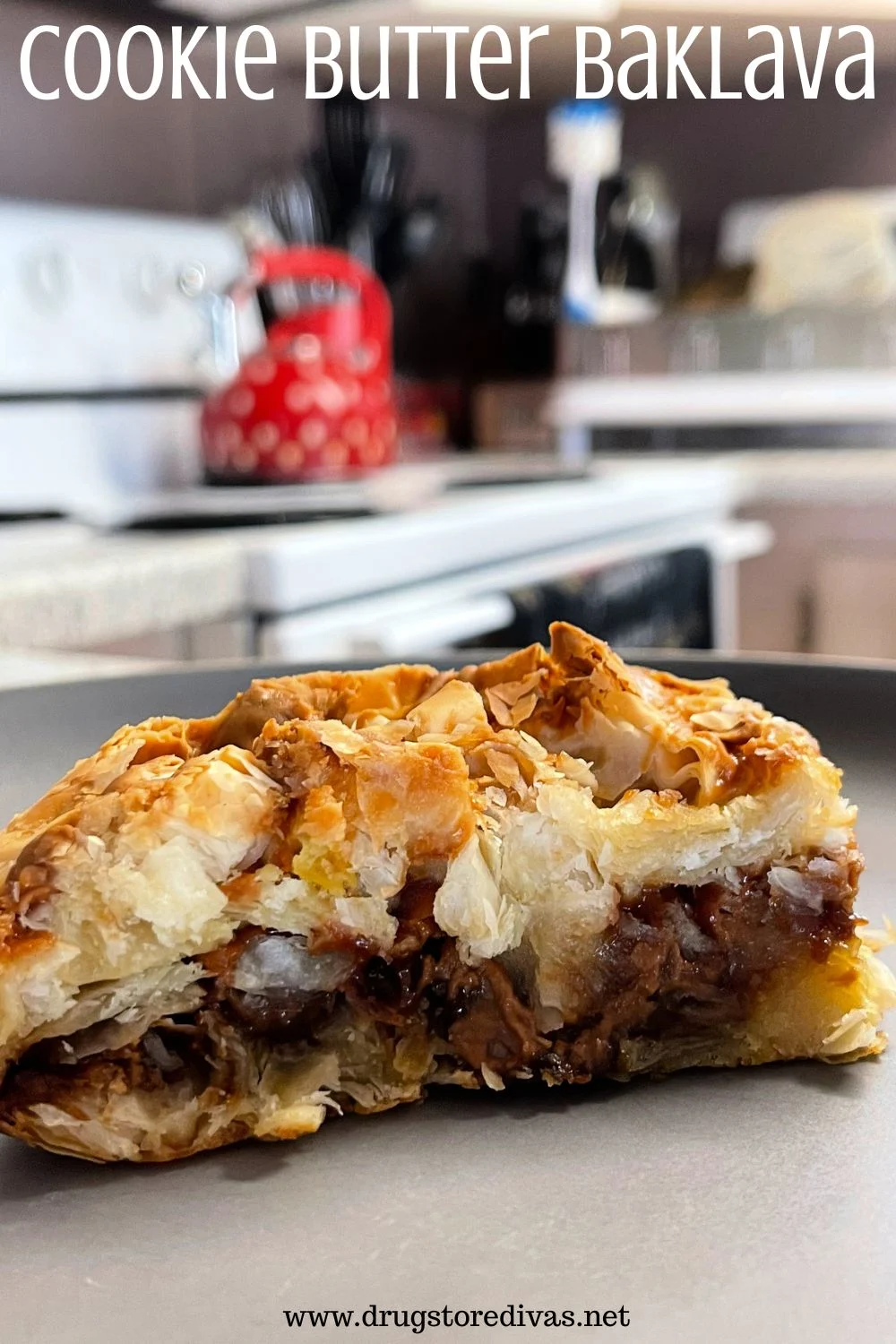A piece of layered pastry on a plate with a kitchen behind it and the words