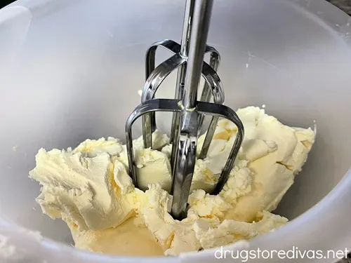 Cream cheese in a clear bowl with electric beaters in it.