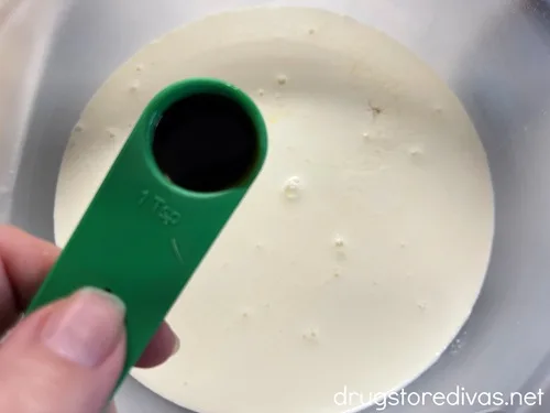 Vanilla in a measuring spoon being added to a bowl filled with heavy cream.