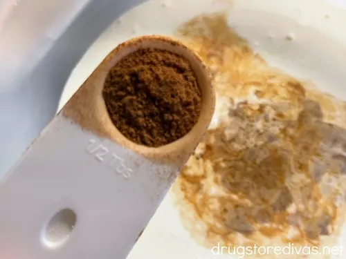 Cinnamon in a white measuring spoon being added to a bowl filled with heavy cream.