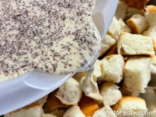 Custard in a white bowl being poured over cubes of Hawaiian rolls.