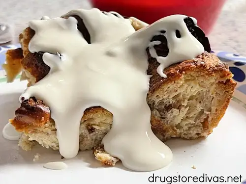 A piece of hawaiian roll bread pudding with thick white sauce on top on a white plate.