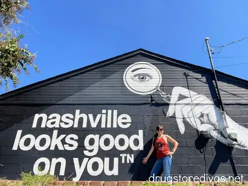 A woman in a maroon tank top in front of a building with a mural that says "Nashville Looks Good On You" in Marathon Village in Nashville.