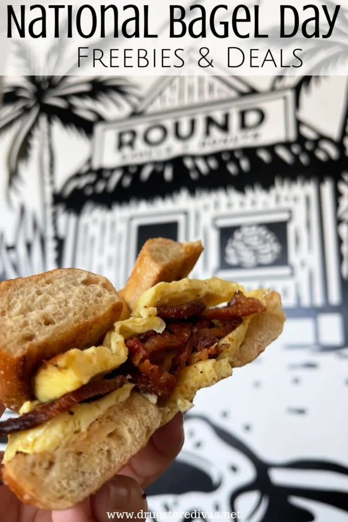A hand holding a bacon, egg, and cheese bagel sandwich with the words "National Bagel Day Freebies & Deals" digitally written above it.