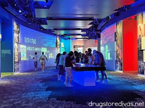 The Rivers of Rhythm corridor, with people and tables in the middle and images projected on the walls, in the National Museum of African American Music in Nashville.