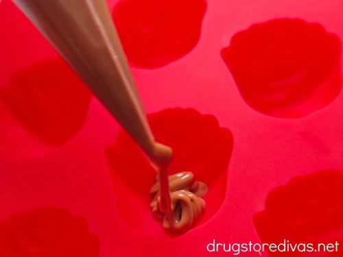 Melted chocolate in a piping bag being piped into a rose-shaped silicone mold.