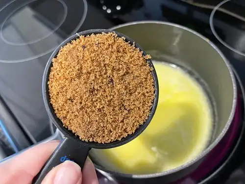 Brown sugar in a measuring cup above a pot with melted butter in it.