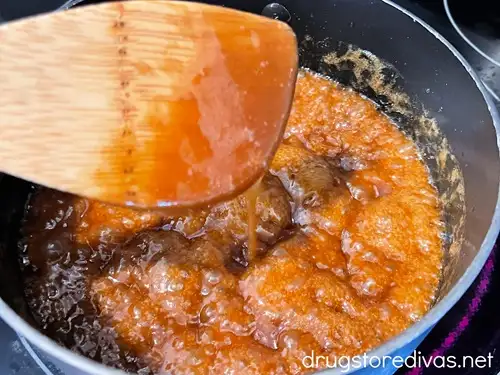 A bamboo spoon above a pot of sticky toffee caramel.