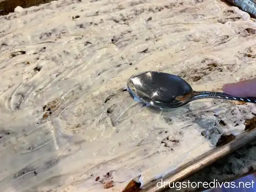 A spoon spreading white chocolate on crackers in a baking tray.