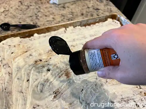 A hand sprinkling a jar of seasoning above a tray of melted white chocolate.