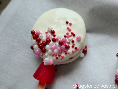 A white chocolate dipped Oreo with circle sprinkles on the bottom half and a red Dot candy at the base.