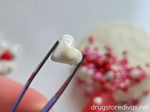 Tweezers holding a heart-shaped sprinkle with a dab of white chocolate on it.
