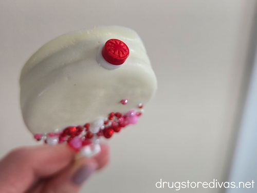 A red flat sprinkle on top of a white chocolate dipped Oreo cookie that has other sprinkles on it.
