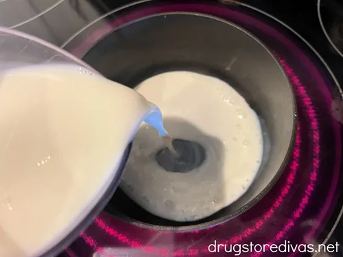 Milk being poured into a stockpot on a stove.
