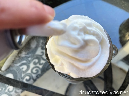 A hand putting canned whipped cream on a drink.