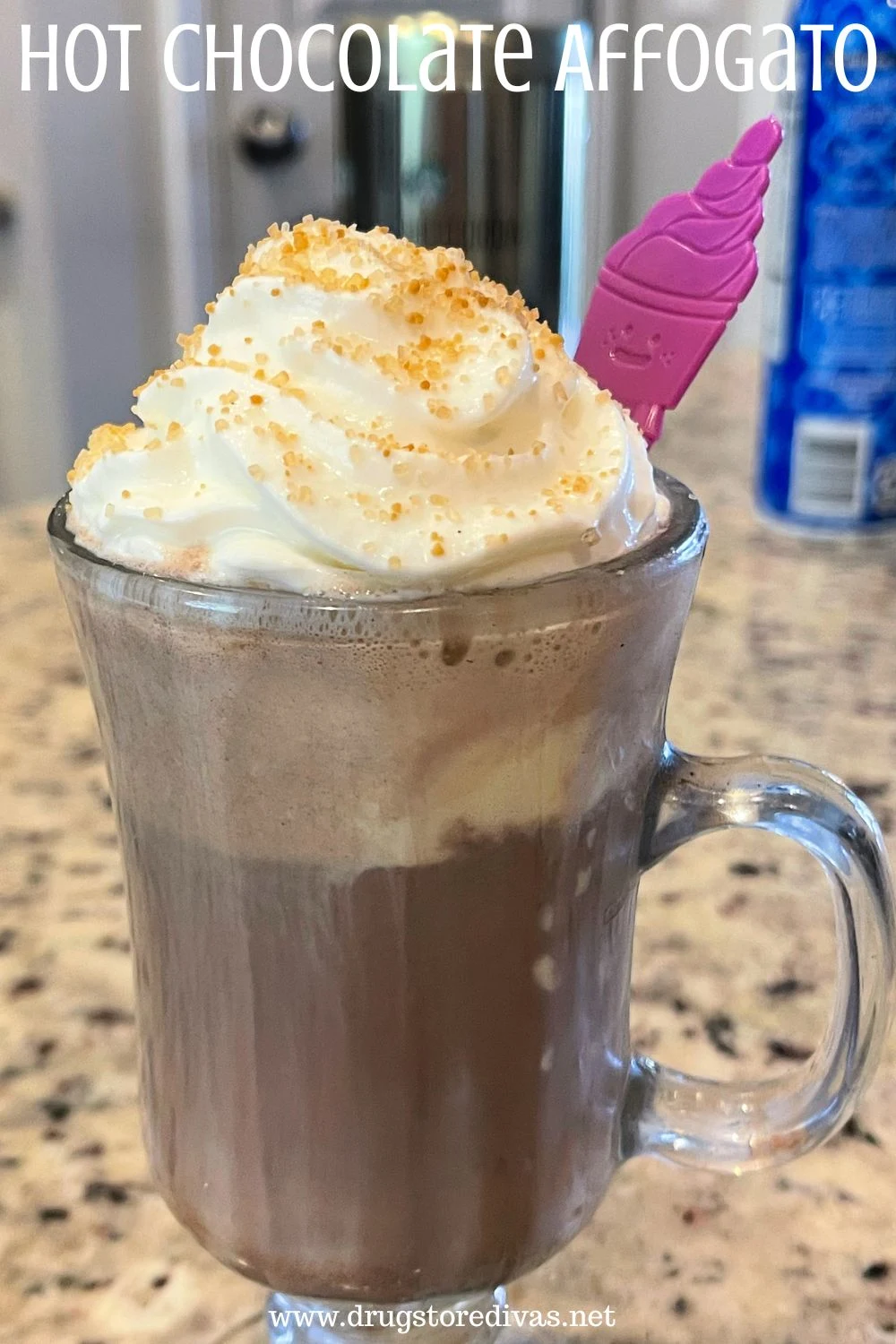 Hot chocolate with whipped cream in a glass with a purple spoon out the top and the words 