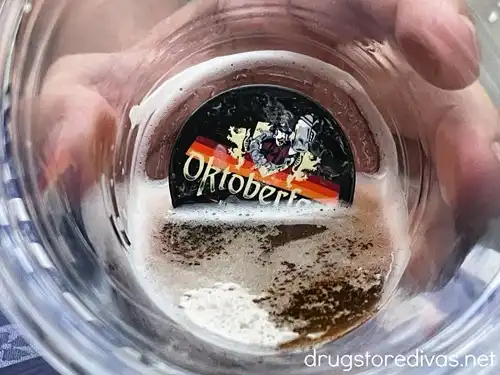 A hand holding a cup with a little bit of beer in it and an Oktoberfest charm at the bottom.
