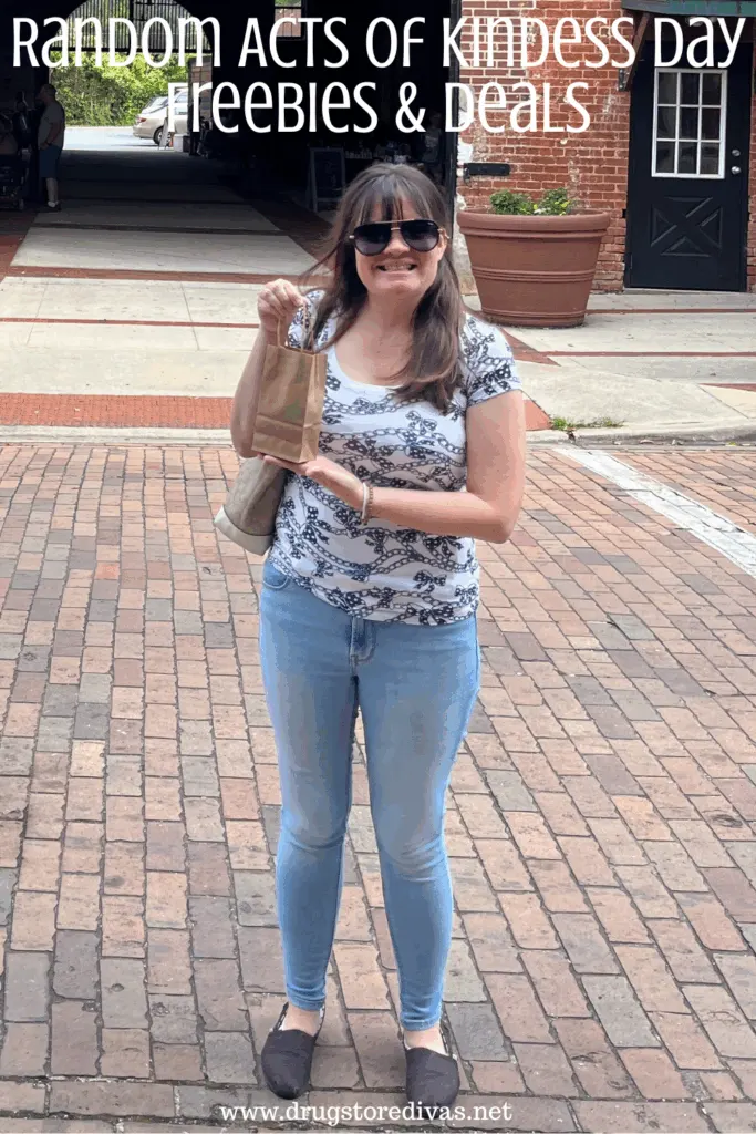 A woman holding a gift in a brown bag on a brick road in front a building with the words "Random Acts Of Kindness Day freebies and deals" digitally written above her.