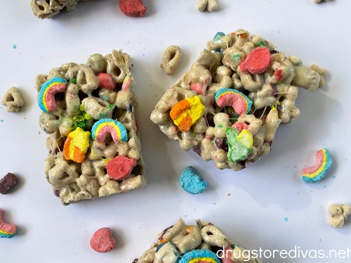 Two Lucky Charms marshmallow treats on a white tray surrounded by cereal and marshmallows.