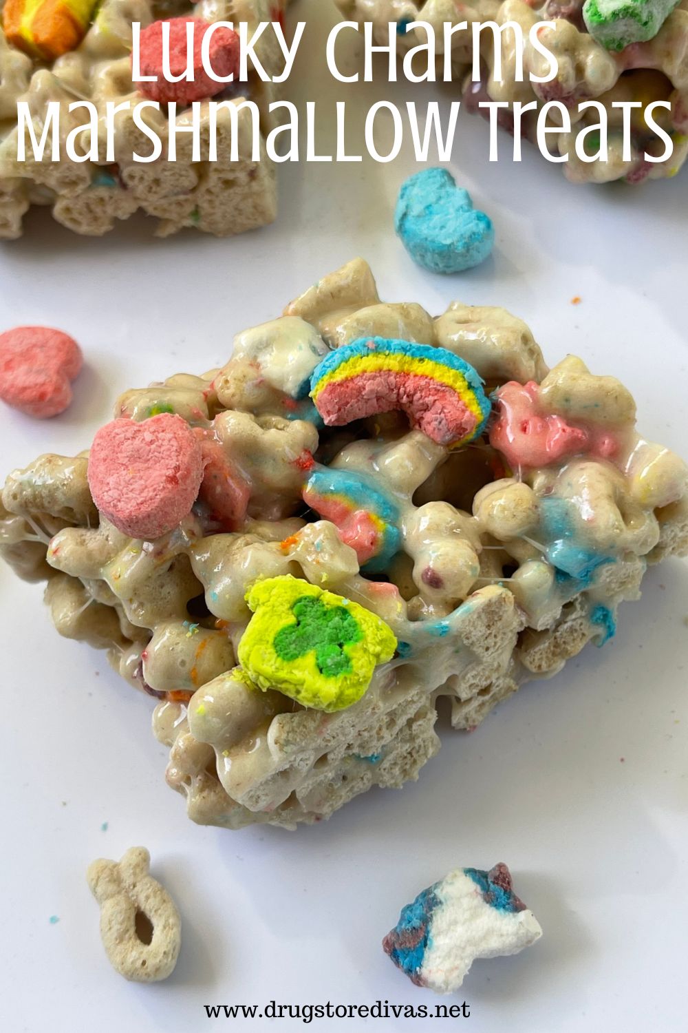 A marshmallow cereal treat on a white board with two behind it and cereal and marshmallows around it with the words 