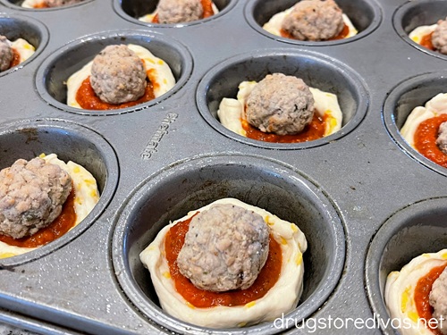 Frozen meatballs on top of marinara sauce on top of biscuit pieces in a muffin pan.