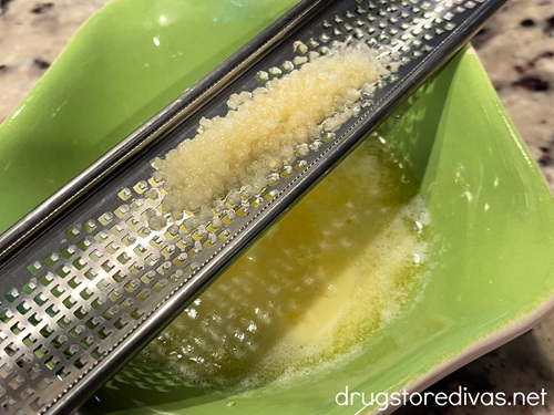 Garlic on a microplane grater above melted butter in a green bowl.