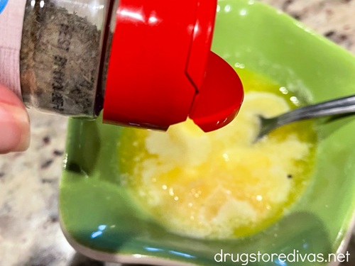 A bottle of seasoning about to be poured into melted butter in a green bowl.