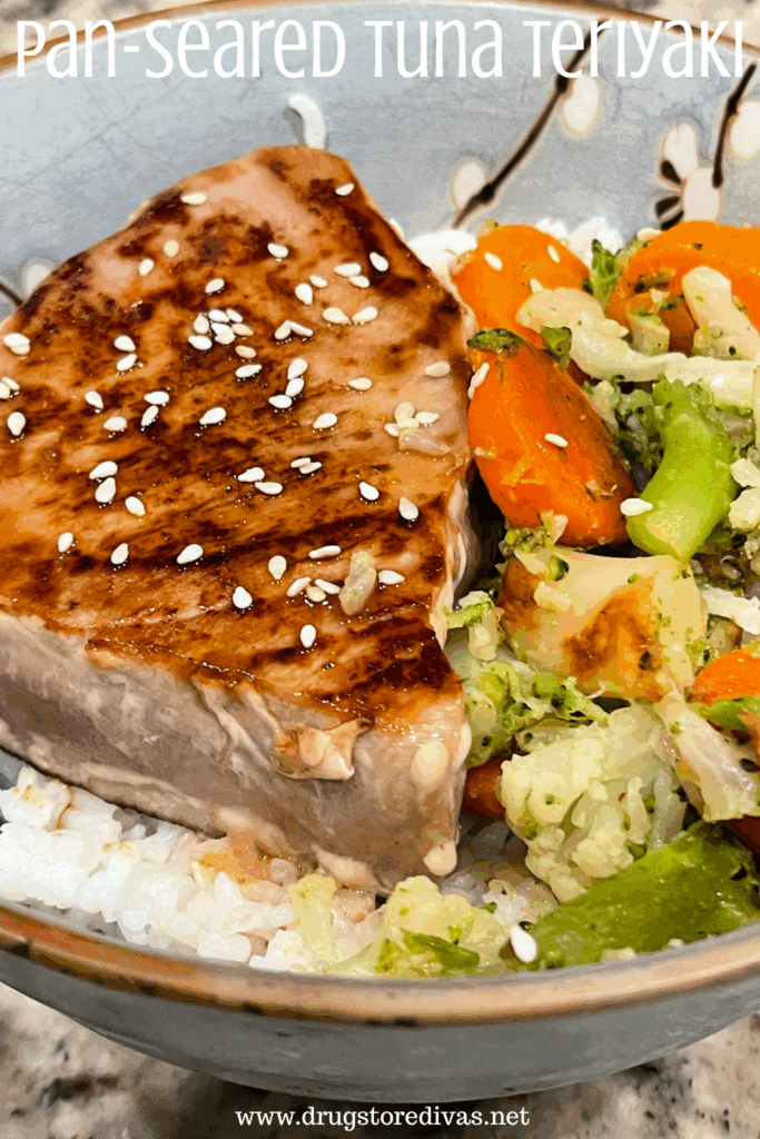 A piece of tuna steak with sesame seeds on it next to vegetables on top of rice in a blue bowl with the words "Pan-Seared Tuna Teriyaki" digitally written on top.