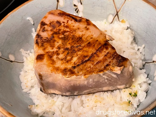 A cooked tuna steak on top of white rice in a blue bowl.