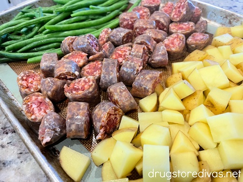 Green beans, cut sausage rounds, and cubed potato on a sheet pan.